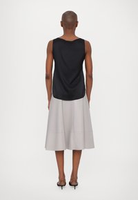 Black satin sleeveless top with a curved hem, paired with a light gray pleated midi skirt and strappy black heeled sandals.