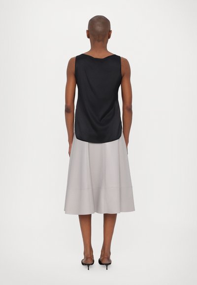 Top senza maniche in satin nero con orlo curvo, abbinato a una gonna midi plissettata grigia chiara e sandali con tacchi neri e cinturini.