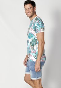 Camiseta de manga corta en blanco con estampado colorido de hojas de palmera. Combinada con pantalones cortos de denim azul claro, con dobladillo enrollado.