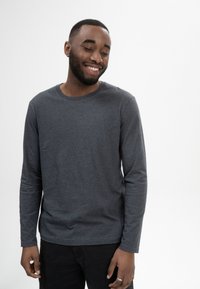 Grau langärmliges T-Shirt aus weichem Stoff mit rundem Halsausschnitt und lässiger Passform, kombiniert mit dunklen Hosen. Minimalistisches Design.