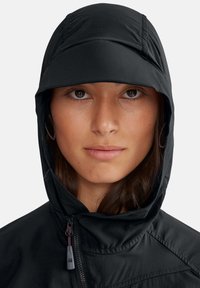 Veste à capuche noire avec une surface texturée, fermeture à glissière sur le devant et détails de couture. La capuche est ajustée autour du visage.