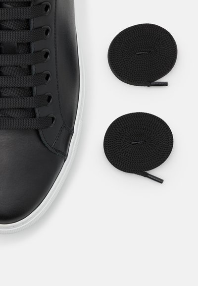 Black leather sneaker with white rubber sole, featuring black laces and two additional round black shoelaces beside it.