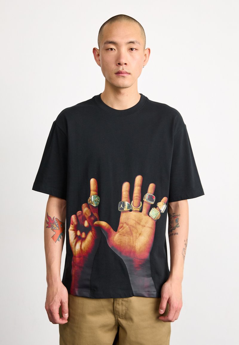 Černé krátké tričko s potiskem dvou rukou s prsteny. Vyrobeno z bavlny, s volným střihem a živými designovými detaily.