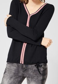 Svart långärmad topp med rosa detaljer längs V-ringningen och sidsömmarna; justerbar dragsko i nederkant. Strukturerad tyg med avslappnad passform.