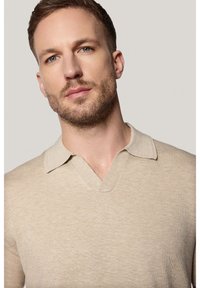 Beżowy sweter z dekoltem w serek i kołnierzykiem, wykonany z teksturowanej dzianiny. Zbliżenie na wzór i kolor odzieży.