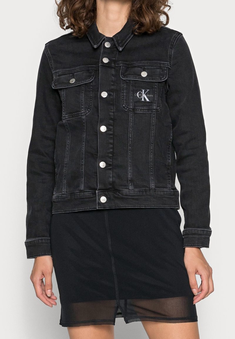 Svart jeansjacka med silverfärgad hårdvara, innehållande framfickor, knappstängning och en Calvin Klein-logotyp på vänster bröst.