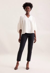 White V-neck blouse with puff sleeves, textured fabric, paired with black slim-fit pants and strappy heels for a modern look.