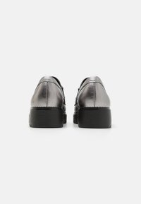 Metallisch zilveren leren schoenen met een ronde neus, zwarte rubberen zool en stikdetails. Het uitzicht van achteren toont een gladde textuur en een stevige hak.