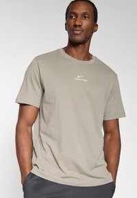 Λιγότερο έντονο ελιάς πράσινο T-shirt Nike Pro με κοντά μανίκια, στρογγυλή λαιμόκοψη και διακριτικό λογότυπο στο στήθος. Λείο ύφασμα με άνετη εφαρμογή.