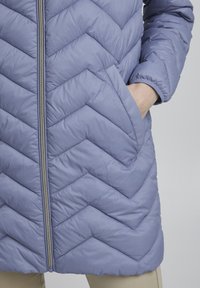 Giacca trapuntata di un leggero colore viola, con un motivo a zigzag, cerniera centrale e tasche laterali, realizzata in un materiale morbido e lucido.