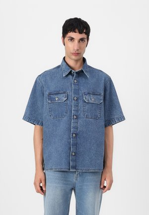 Denim short-sleeve shirt in light blue, featuring a button front, two chest pockets, and a relaxed fit. Smooth texture with visible stitching.