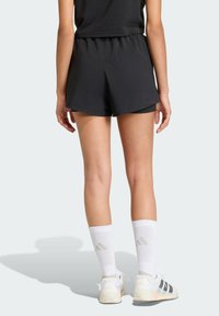 Pantalones cortos deportivos negros con un ajuste relajado y banda elástica en la cintura, combinados con calcetas blancas hasta la rodilla y zapatillas de tenis con acentos negros.