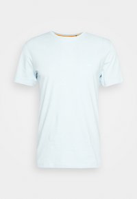 T-shirt en coton bleu clair avec un col rond, des manches courtes et un petit patch logo sur la poitrine. Texture lisse, coupe décontractée.