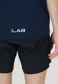 Meripaidan urheilupaita, jossa on "ELITE LAB" -logo, yhdistettynä mustiin shortseihin. Sileä pinta, muotoon ommeltu malli ja yksinkertainen väriteema.