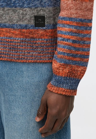 Pletený svetr s vícestrannými pruhy v oranžové, modré a šedé barvě s žebrovanými manžetami. Malá černá etiketa s nápisem "PS Paul Smith" viditelná na spodním lemu.