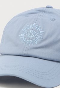 Ανοιχτό μπλε καπέλο του μπέιζμπολ με κεντημένο λευκό μάτι περιτριγυρισμένο από ακτίνες ήλιου στην μπροστινή πλευρά.