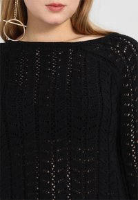 Maglione nero lavorato a maglia con un motivo a traforo, caratterizzato da texture orizzontali e verticali e un ampio scollo.