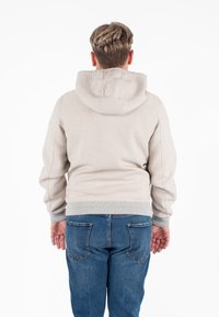 Felpa beige con cappuccio, maniche lunghe e polsini a coste, abbinata a jeans blu scuro. Tessuto morbido e vestibilità casual.