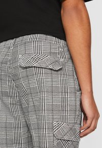 Schwarz-weiße karierte Cargo-Hosen mit seitlichen Taschen und einem strukturierten Stoff. Sie verfügen über einen eng anliegenden Bund und sichtbare Nähdetails.