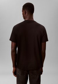 Zwart T-shirt met korte mouwen gemaakt van zachte stof, met een klassieke ronde halslijn en een losse pasvorm. Achteraanzicht toont een gladde textuur en strakke lijnen.