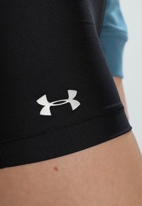 Czarne sportowe szorty o dopasowanym kroju, gładkiej fakturze i odblaskowym srebrnym logo Under Armour na dolnej części nogawki.