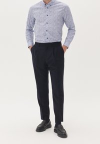 Ljusblå skjorta med knäppning och blommönster, matchad med skräddarsydda marinblå byxor och svarta loafers. Slät tyg, strukturerad design.