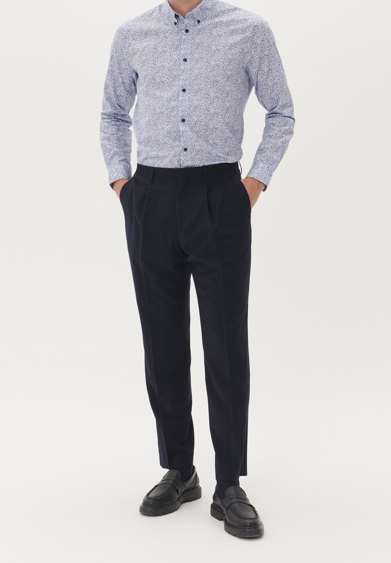 Ljusblå skjorta med knäppning och blommönster, matchad med skräddarsydda marinblå byxor och svarta loafers. Slät tyg, strukturerad design.