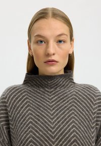 Maglione dolcevita marrone e beige con motivo a spina di pesce, realizzato in morbido materiale a maglia, caratterizzato da un collo alto e una vestibilità comoda.