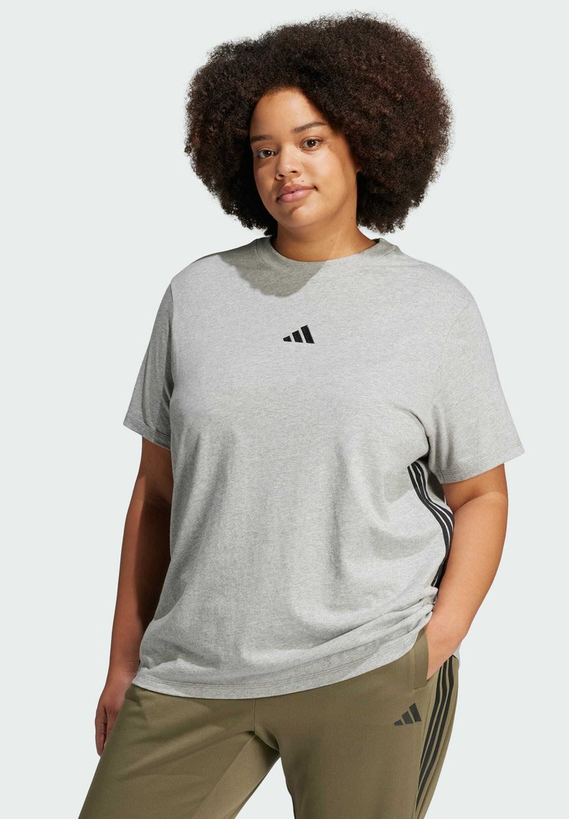 Camiseta de algodón gris con mangas cortas, cuello redondo y logo negro de Adidas. Combinada con pantalones verdes oliva que cuentan con franjas laterales negras.