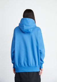 Hoodie i klarblått, tillverkad av mjukt bomullsmaterial. Har en avslappnad passform, ribbade muddar och fåll samt en rymlig huva.