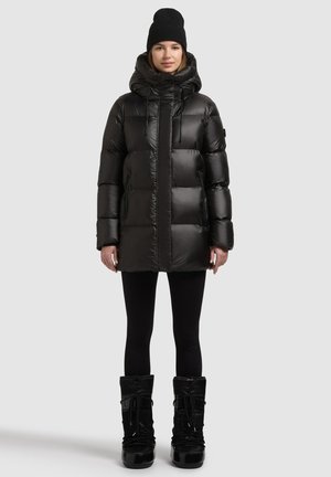 Black puffer jacket with a high collar, drawstring hood, and zippered pockets, paired with black leggings and snow boots. Smooth, shiny texture.
