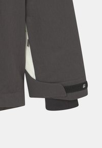 Grau Jackenärmel mit strukturiertem Stoff, Klettverschluss am Bund, kontrastierendes weißes Futter sichtbar, scharfes, tailliertes Design.