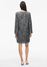 Īsām piedurknēm sudraba mirdzoša kleita ar brīvu piegriezumu, apaļu kakla izgriezumu un ceļgala garumu, papildināta ar gludiem sandāļiem.