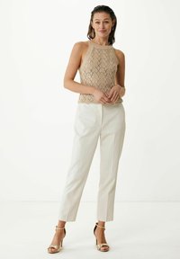 Beige stickad halter-top med ett geometriskt mönster, kombinerad med vita skräddarsydda byxor och guldankelremmar. Släta texturer, åtsittande design.