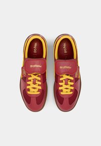 Gryffindor tematikas sporta apavi ar sarkanu sintētisko materiālu, dzeltenām auklām un Velcro siksnu ar zīmolu uz sāniem un iekšzoles.