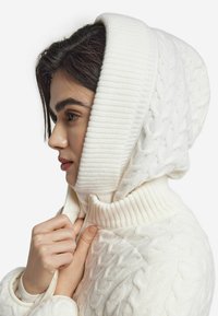 Biała dzianinowa bluza z kapturem z warkoczowym wzorem, z grubym ściągaczem przy kołnierzu i kapturze. Tekstura jest miękka, a dopasowanie wokół szyi jest przylegające.