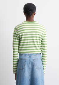 Groene en witte gestreepte lange mouw shirt, plat breisel, ronde hals, gecombineerd met een hoog gewaisted spijkerrok, zichtbare achterzakken.
