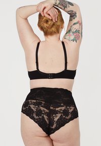 Zwarte kant hoge taille slip en bijpassende bralette. Het ontwerp heeft bloemmotieven, verstelbare bandjes en een gestructureerde kanten afwerking.