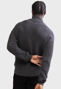 Dark gray knitted sweater with a high collar and ribbed texture. Features long sleeves and a relaxed fit, viewed from the back.