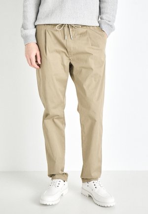Beige, lightweight trousers with a drawstring waist and cuffed hems. Paired with white lace-up shoes and gray ribbed sweater.