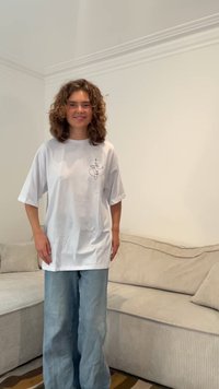 Camiseta blanca de gran tamaño con mangas cortas, que presenta un dibujo de línea negra simple en el lado izquierdo del pecho. Combinada con jeans de pierna ancha en azul claro.
