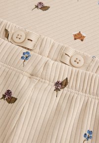 Lys beige bomuldsstof med ribbet tekstur, prydet med små blomster mønstre i lilla og blå, samt to beige knapper i taljen.
