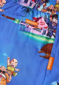 Mėlynos maudymosi šortai su ryškia personažų ir Kame House iliustracija, šoninėje dalyje su oranžine Opposuits etikete.