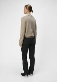 Suéter beige de manga larga con escote redondeado, combinado con jeans negros de pierna recta y tacones negros puntiagudos, visto desde atrás.