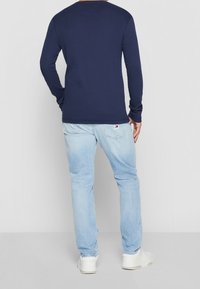 Navy long-sleeve shirt with a crew neckline, paired with light blue jeans and white sneakers, showing a relaxed fit and cuffed sleeves.