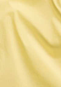 Tessuto giallo chiaro con una consistenza liscia, caratterizzato da morbide pieghe e sottili grinze, creando delicati contorni sulla superficie.