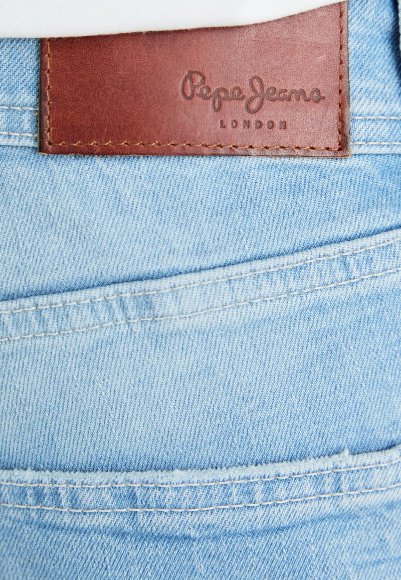 Helle blaue Denim-Jeans verfügen über einen braunen Lederaufnäher auf der Rückseite, der mit "Pepe Jeans London" geprägt ist, und zeigen Details der Nähte sowie die Naht der Taschen.