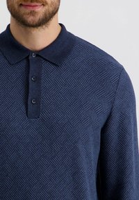 Marineblaues Langarm-Polo-Shirt mit strukturiertem Rautenmuster, Kragen und Knopfverschluss mit drei Knöpfen.