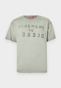 Ανοιχτό γκρι T-shirt Diesel με ξεθωριασμένο μαύρο κείμενο "PROPERTY OF D.I.E.S.E.L" ανάποδα στο μπροστινό μέρος και κόκκινη ετικέτα με το λογότυπο μέσα στο γιακά.