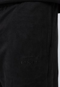 Pantalones jogger negros fabricados en un tejido suave, con un ligero brillo, y que cuentan con un logotipo bordado "PXP" en el costado en negro a juego.